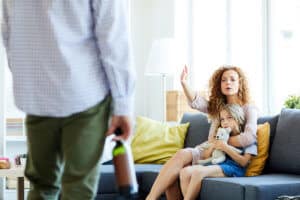 a woman holds her daughter as she tells her husband how his addiction affects the whole family