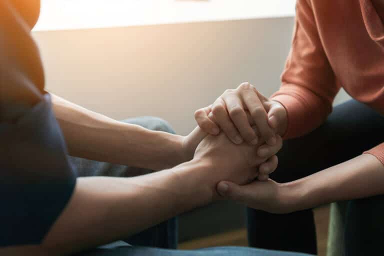 two people sit across from each other while clasping hands in a relapse prevention plan