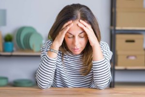 stressed out woman resting elbows on table while holding temples and wondering is addiction a disease