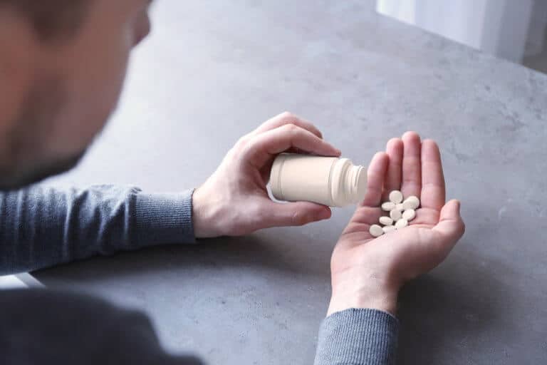 man emptying pill bottle into his hand, pill popping prescription drug abuse