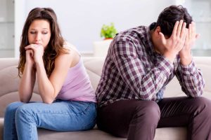 unhappy woman sitting next to man with head in his hands as signs of codependency